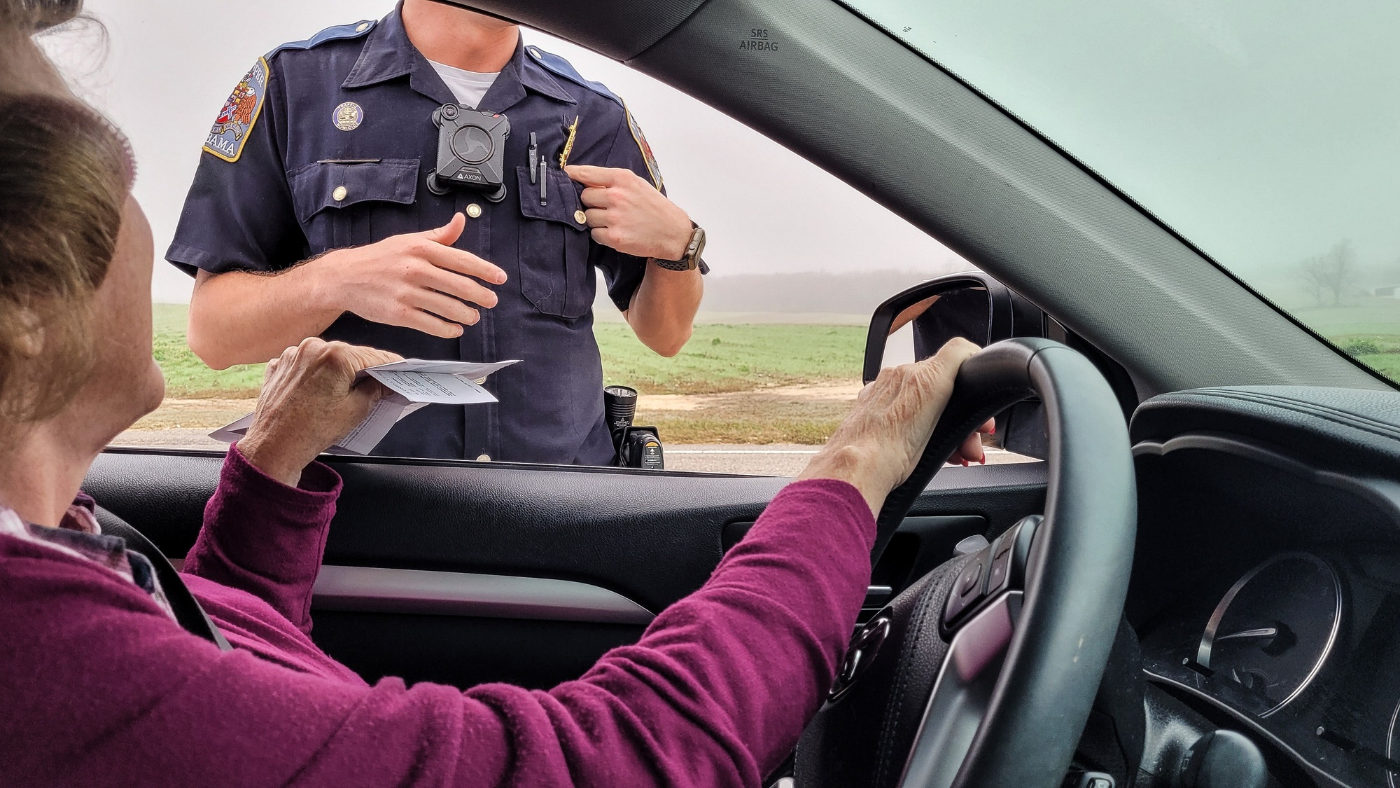 Senior woman stopped for speeding hands her car registration through a window to waiting Policeman.